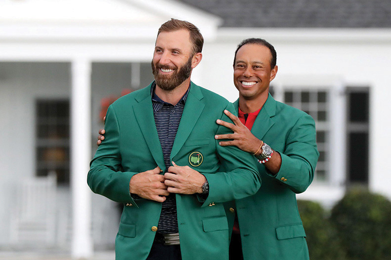 Last year's Masters champion Tiger Woods (right) presents Dustin Johnson his first green jacket after winning the Masters Tournament Sunday, Nov. 15, 2020 at Augusta National in Augusta, Georgia. (Curtis Compton/Atlanta Journal-Constitution/TNS)